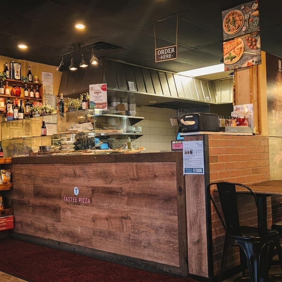 Interior of Tastee Pizza restaurant with a wooden counter, brick walls, and a beverage cooler.