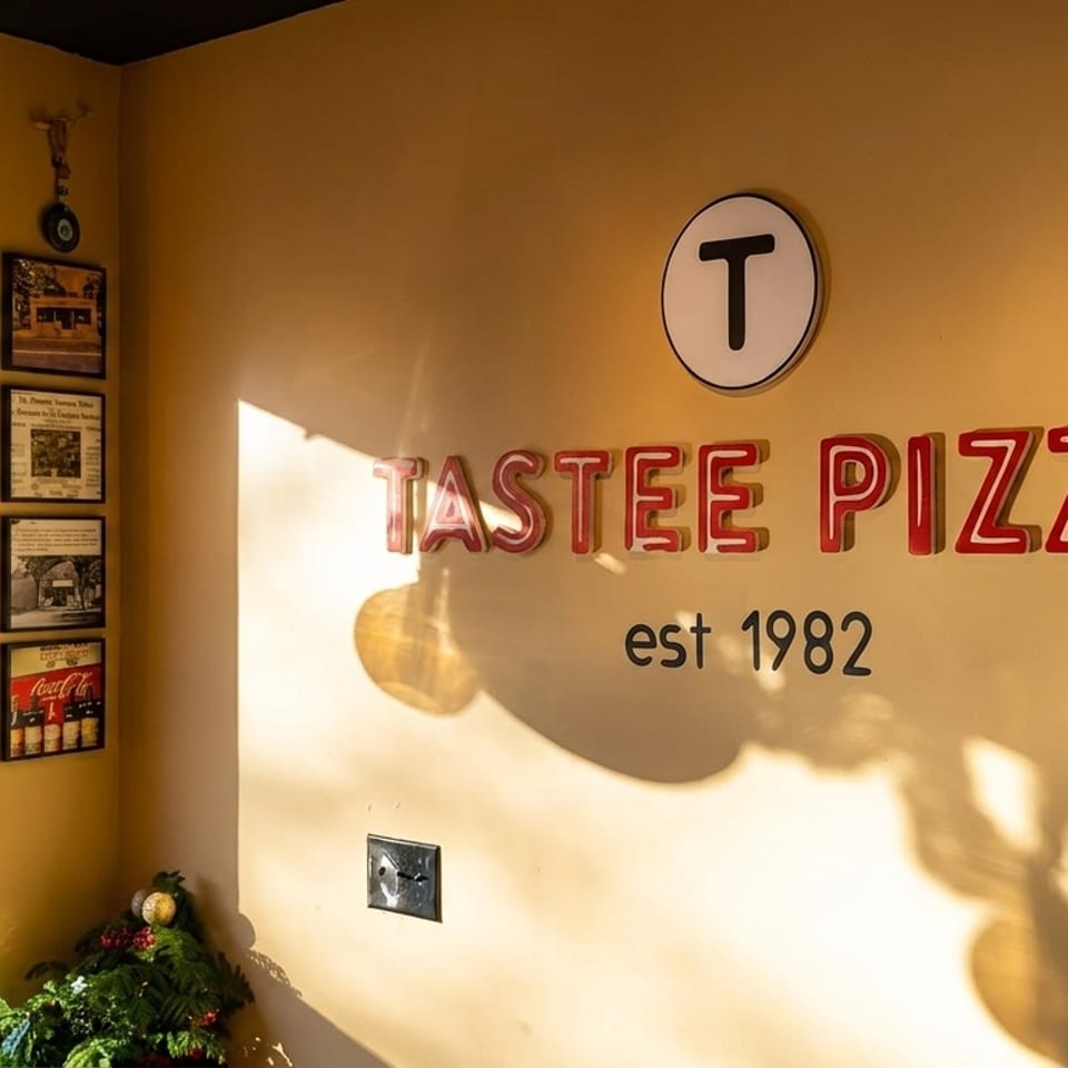Sunny interior of Tastee Pizza restaurant with red neon sign, framed photos, and window view.